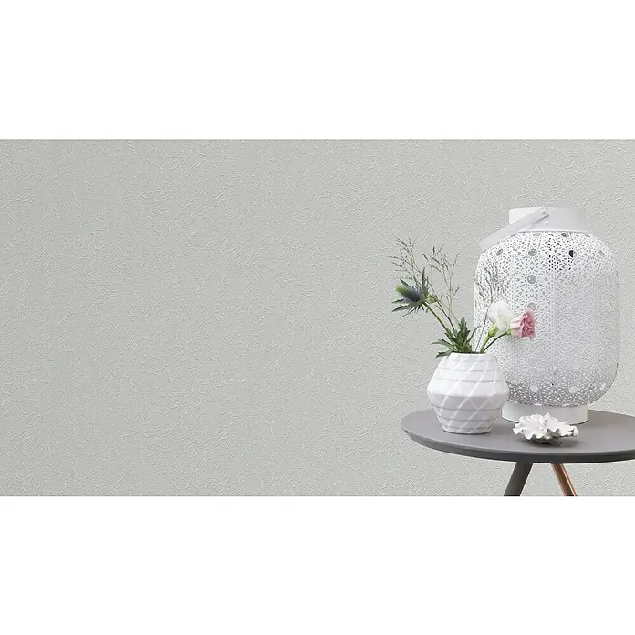 Rasch Wallton Vliestapete Strukturierte Putzoptik - Weiß, Uni, 10,05 x 0,53 m, Grobe Struktur, Glänzend - Nahaufnahme einer Tischdekoration mit weißer Vase, Blumen, einer verzierten Laterne und einer kleinen Dekoschale, arrangiert auf einem grauen Beistelltisch.