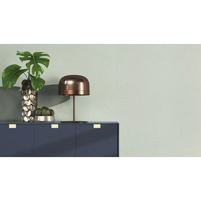 Rasch Bambino XIX Vliestapete - Salbei, Uni, 10,05 x 0,53 m - Elegante Kommode in dunklem Blau mit goldenen Griffen, dekoriert mit einer stilvollen Lampe, einer Monstera-Pflanze und Kakteen.