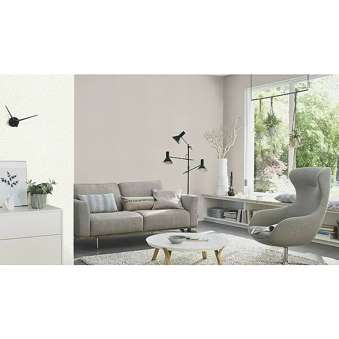 Rasch Bambino XIX Vliestapete - Hellgrau, Uni, 10,05 x 0,53 m - Modernes Wohnzimmer mit hellbeiger Struktur-Tapete und dezenter gepunkteter Akzentwand, möbliert mit grauem Sofa und bequemem Sessel.