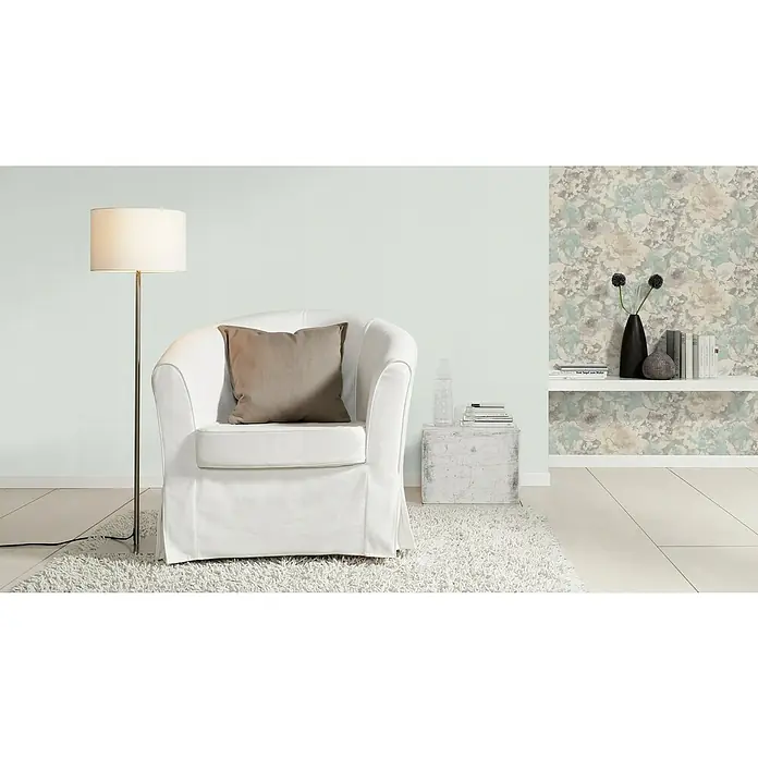 Rasch Salsa Vliestapete Textilstruktur - Mint, Uni, 10,05 x 0,53 m - Einladender Sessel mit beigem Kissen unter Stehlampe. Dekorative Wand im Hintergrund. Stilvolle Wohnraumgestaltung mit weißem Sessel und Textilien.