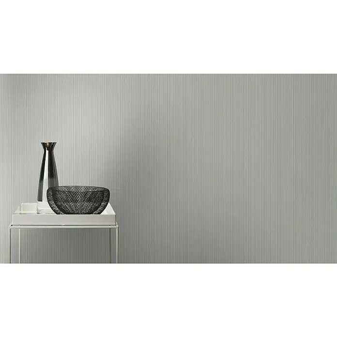 Rasch Selection Vliestapete - Grau, Uni, 10,05 x 0,53 m - Elegante Tischdekoration: eine schmale Glasvase und eine schwarze Drahtschale auf einem weißen Tisch, vor einem Hintergrund mit feinen vertikalen Linien.