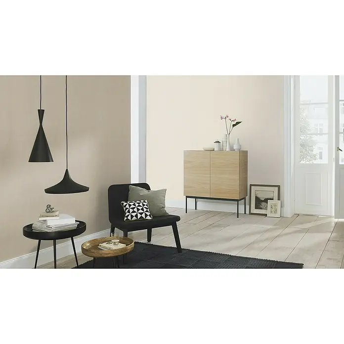 Rasch Salsa Vliestapete - Beige, Uni, 10,05 x 0,53 m - Stilvolles Wohnzimmer mit modernen Pendelleuchten, einem schwarzen Sessel und einem hellen Holzschrank für ein elegantes Ambiente.