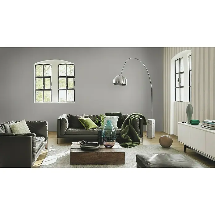 Rasch Salsa Vliestapete Textilstruktur - Dunkelgrau, Uni, 10,05 x 0,53 m - Stilvolles Wohnzimmer mit grauem Ledersofa, dekorativen Kissen und einer eleganten Stehlampe, die eine gemütliche Atmosphäre schafft.