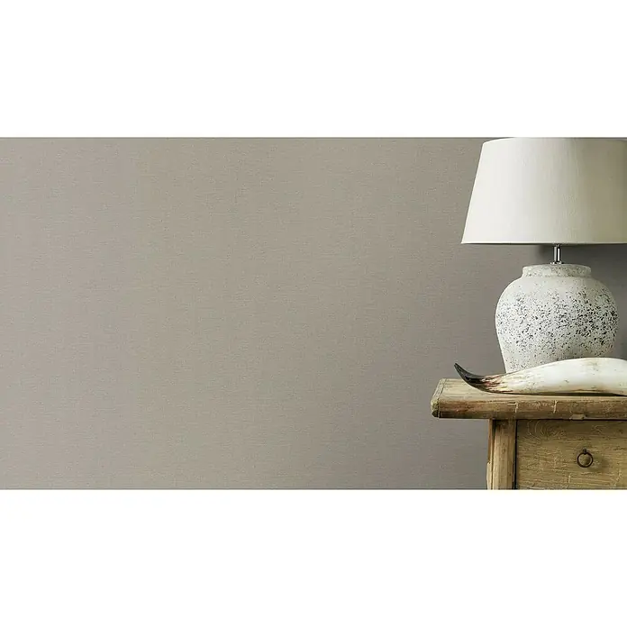 Rasch Salsa Vliestapete - Grau, Uni, 10,05 x 0,53 m - Tischleuchte mit weißem Schirm und einem dekorativen Horn auf einem rustikalen Holztisch. Die Lampe strahlt ein warmes, einladendes Licht aus.