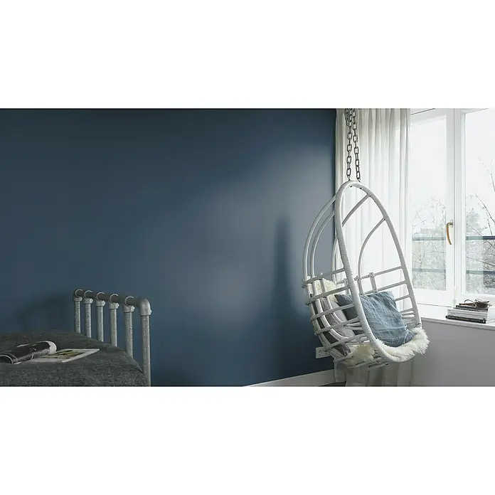 Rasch Salsa Vliestapete - Dunkelblau, Uni, 10,05 x 0,53 m - Ein helles Zimmer mit einem Hängekorbsessel, der mit einem Kissen und einem Fell ausgestattet ist, neben einem Fenster mit Büchern.