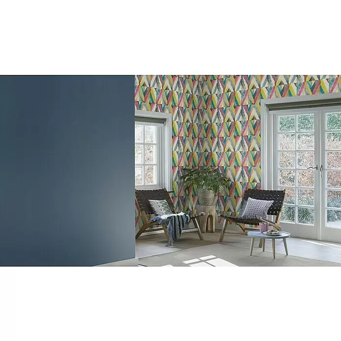 Rasch Salsa Vliestapete - Dunkelblau, Uni, 10,05 x 0,53 m - Bunte geometrische Tapete mit Dreiecksmuster an einer Akzentwand in einem gemütlichen Wohnbereich mit Möbeln und Fenstern.