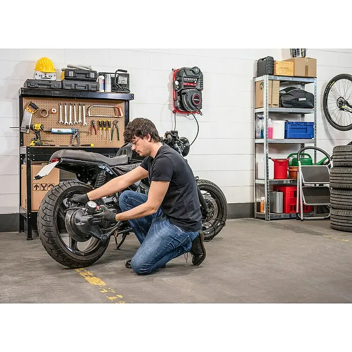 Herkules Kompressor Walltech Pro - Max. Druck: 8 bar, 2 l - Ein Mann überprüft den Reifendruck eines Motorrads in einer Garage, wobei ein HERCULES-Luftkompressor an der Wand montiert ist.