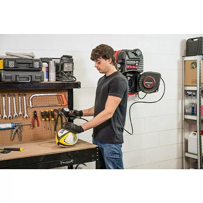 Herkules Kompressor Walltech Pro - Max. Druck: 8 bar, 2 l - Mann in einer Werkstatt pumpt einen Rugbyball mit einem roten und schwarzen HERKULES Kompressor und Inflator auf.