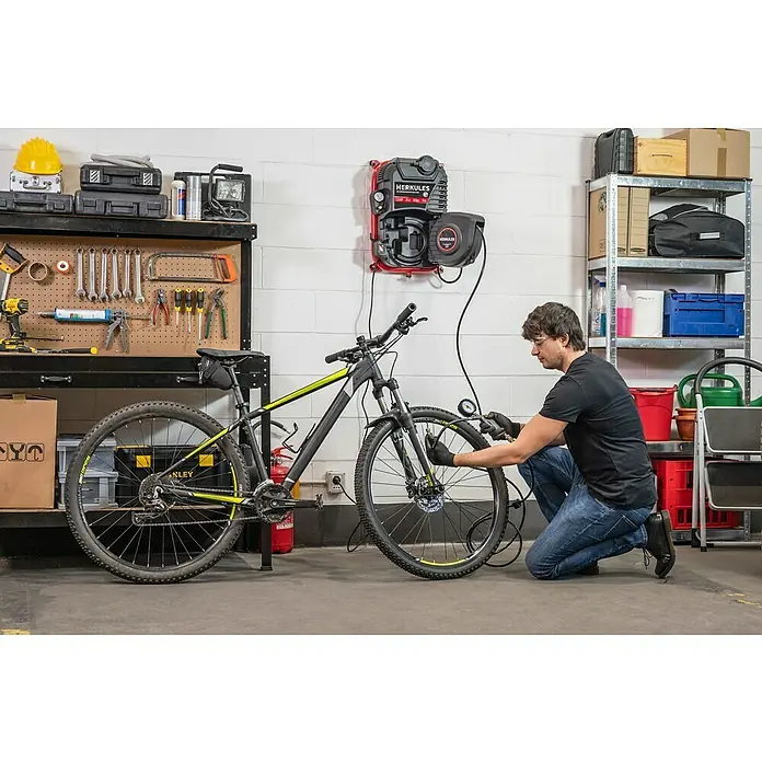 Herkules Kompressor Walltech Pro - Max. Druck: 8 bar, 2 l - Ein Mann pumpt mit einem Herkules-Luftkompressor einen Fahrradreifen in einer Garage auf. Werkzeuge und Regale sind im Hintergrund zu sehen.