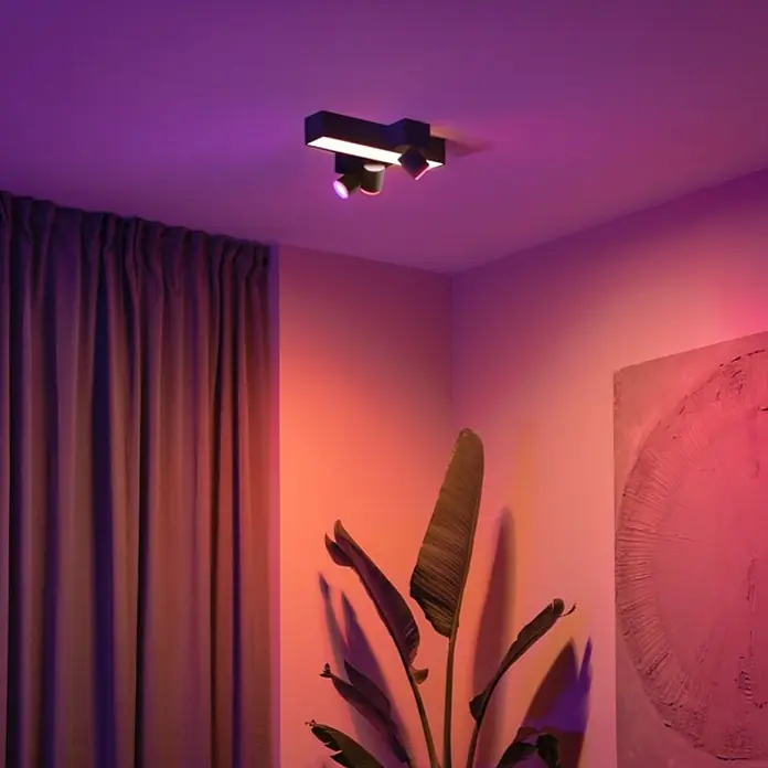 Philips Hue LED-Deckenstrahler Centris25 W, L x B x H: 40,8 x 33,7 x 12,8 cm, Schwarz, Mehrfarbig - Deckenleuchte mit drei Strahlern in einem Zimmer mit lila und orangefarbener Beleuchtung.