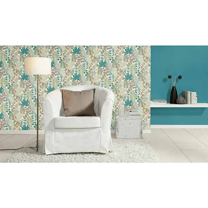 Rasch Salsa Vliestapete Blätter - Creme-Grün, Floral, 10,05 x 0,53 m - Detailansicht eines Raumes mit einem weißen Sessel, einer Stehlampe und einer Wand mit blumigem Muster. Die Kombination aus Möbeln und Wandmuster schafft eine gemütliche Atmosphäre.