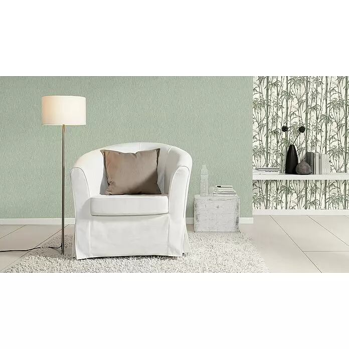 Rasch Florentine III Vliestapete Textile Stoffoptik - Salbei, Uni, 10,05 x 0,53 m - Ein gemütlicher Raum mit zwei Tapeten: einer hellgrünen Strukturtapete und einer weißen Tapete mit grünem Bambusmotiv, die eine ruhige Atmosphäre schaffen.