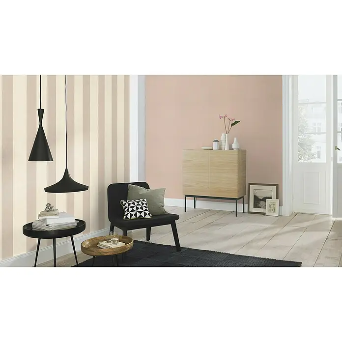 Rasch Florentine III Vliestapete - Rotbeige, Uni, 10,05 x 0,53 m - Einrichtungsidee mit modernen Pendelleuchten, einem schwarzen Sessel und einem hellen Holzschrank vor gestreifter Tapete und rosa Wand.