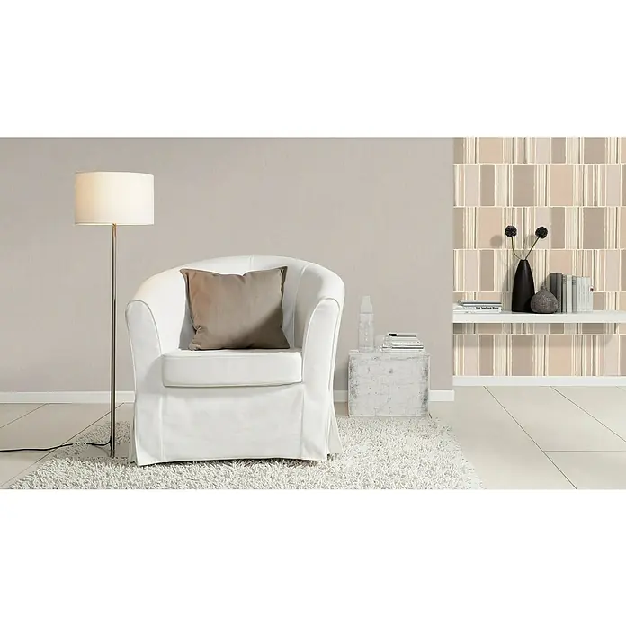 Rasch Florentine III Vliestapete - Hellgrau, Uni, 10,05 x 0,53 m - Das Bild zeigt einen eleganten weißen Sessel mit Kissen, eine Stehlampe und ein Regal mit Dekor vor einer gemusterten Wand.