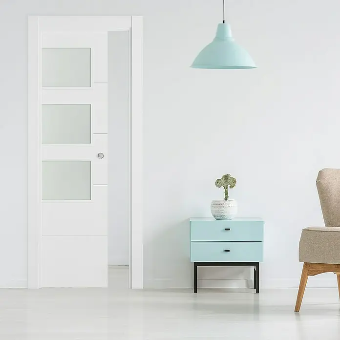 Puerta corredera de madera acristalada Recife - 72,5 x 203 cm, Blanco, Maciza, Con pico de loro - Interior elegante con una puerta blanca moderna con paneles de vidrio, una cómoda azul claro y una lámpara colgante a juego.