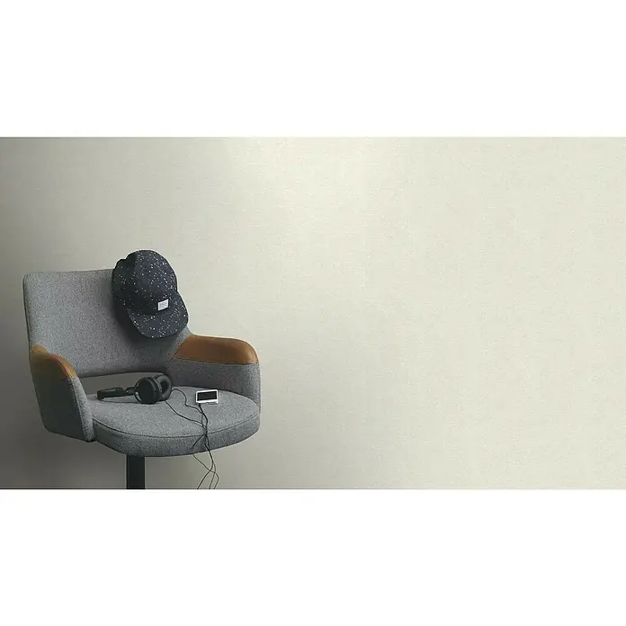 Rasch Tapetenwechsel 2 Vliestapete Textiloptik - Creme, Uni, 10,05 x 0,53 m - Ein grauer Stuhl mit Lederakzenten, auf dem eine Kopfbedeckung, Kopfhörer und ein tragbarer Musikplayer liegen.