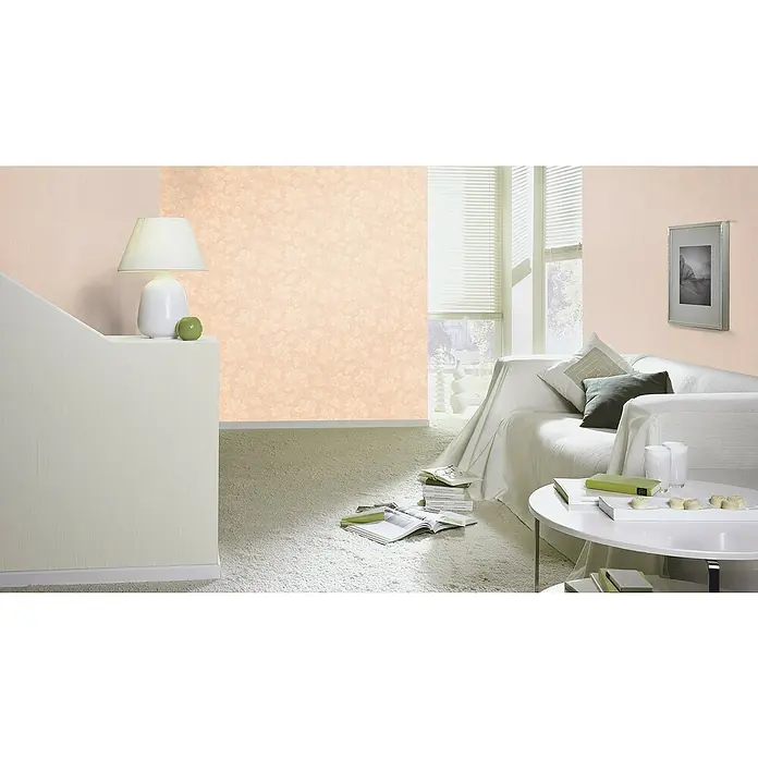 Rasch Trianon XIII Vliestapete Textil - Rosé, Uni, 10,05 x 0,53 m - Ein helles Wohnzimmer mit einem weißen Sofa, einem runden Tisch und einer Lampe. Die Wände sind in einem zarten Pfirsichton gehalten.