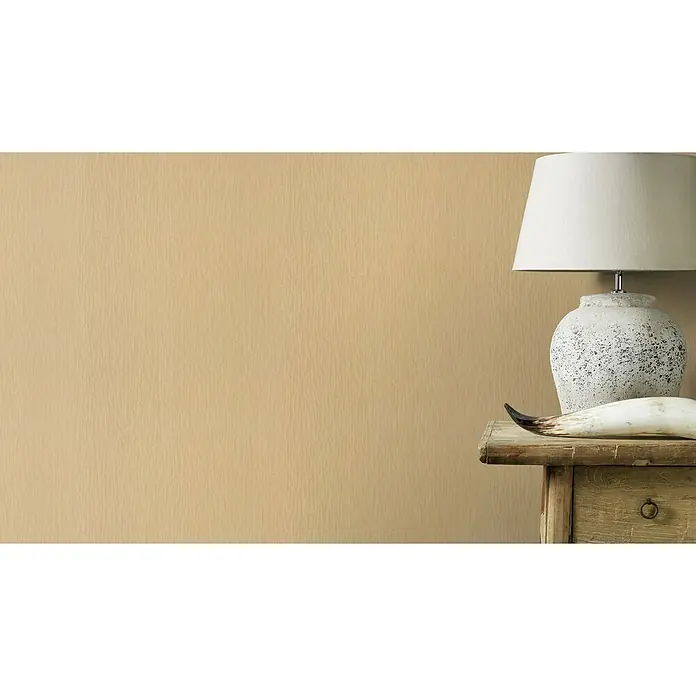 Rasch Trianon XIII Vliestapete Textil - Mattgold, Uni, 10,05 x 0,53 m - Eine elegante Tischlampe mit einem weißen Schirm und einem dekorativen Fuß, platziert auf einem rustikalen Holztisch vor einem warmen, gelblichen Hintergrund.