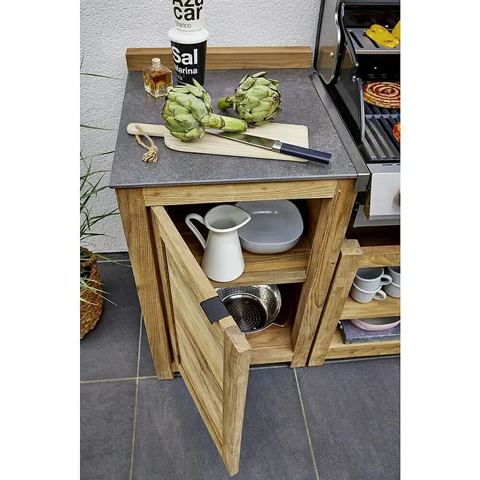 Sunfun Zoe Outdoorküchen-Modul Schrank - Braun, B x T x H: 58 x 63 x 92 cm, Teakholz - Detailaufnahme eines Outdoor-Küchenschranks aus Holz mit geöffneter Tür, Geschirr und Zutaten auf der Arbeitsfläche.