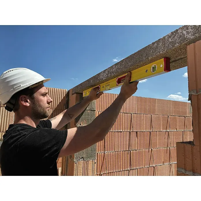 Stabila Wasserwaage Typ 196-2 - Länge: 100 cm, Anzahl Libellen: 3 Stk. - Ein Bauarbeiter mit Schutzhelm benutzt eine gelbe Wasserwaage, um ein Bauelement aus Beton auszurichten. Der Himmel ist blau.