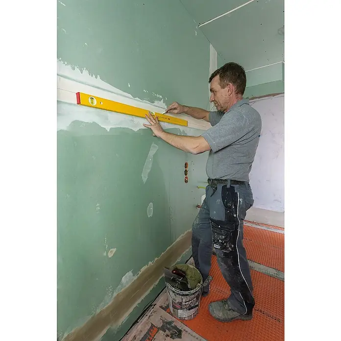 Stabila Wasserwaage 80 AS - Länge: 60 cm, Anzahl Libellen: 2 Stk. - Handwerker nivelliert eine Wand mit einer gelben Wasserwaage. Präzise Messungen für perfekte Ergebnisse im Innenausbau.