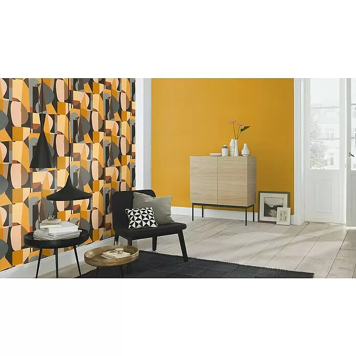 Rasch Tropical House Vliestapete - Curry, Uni, 10,05 x 0,53 m - Modernes Wohnzimmer mit markanter geometrischer Tapete, schwarzen Möbeln und einem hellen Holzschrank an einer gelben Wand.