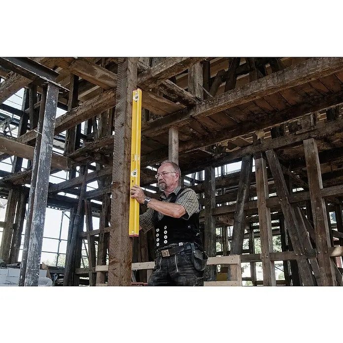 Stabila Wasserwaage Typ R-300 - Länge: 122 cm, Anzahl Libellen: 3 Stk. - Ein Zimmermann prüft mit einer gelben Wasserwaage die Ausrichtung eines Holzbalkens in einem alten Fachwerkhaus.