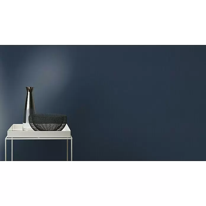 Rasch Tropical House Vliestapete - Nachtblau, Uni, 10,05 x 0,53 m - Weißer Metallbeistelltisch mit weißem Tablett, klarer Glasflasche und schwarzer Drahtgitter-Schale vor dunkelblauer Wand.