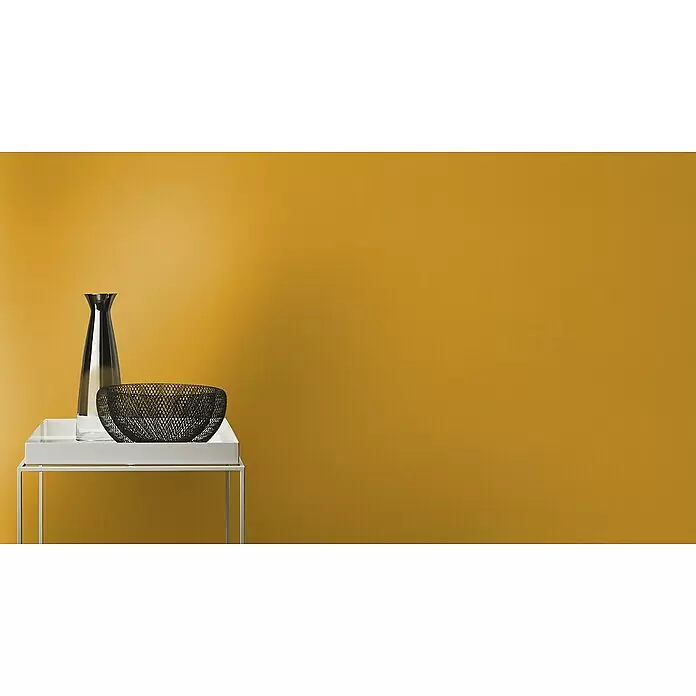 Rasch Tropical House Vliestapete - Curry, Uni, 10,05 x 0,53 m - Ein moderner weißer Metallbeistelltisch trägt eine klare Glasvase und eine schwarze Drahtgeflecht-Dekoschale.