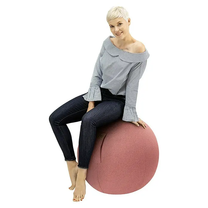 Sitting Ball Gymnastikball Felt - Lachs, Durchmesser: 65 cm, 100 % Polyester - Eine Frau sitzt auf einem pinkfarbenen Sitzball. Der Ball ist aus Stoff und hat eine minimalistische Form. Ideal für gesundes Sitzen.