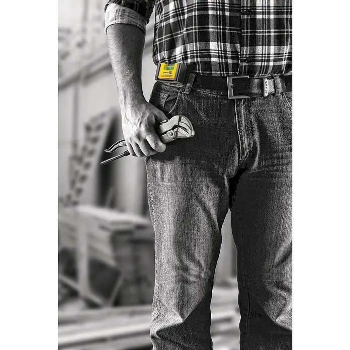 Stabila Wasserwaage Pocket Pro Magnetic - Magnet, Anzahl Libellen: 1 Stk. - Ein Mann in Arbeitskleidung hält eine Rohrzange in der Hand, während er einen gelben Wasserwaagenhalter am Gürtel trägt.