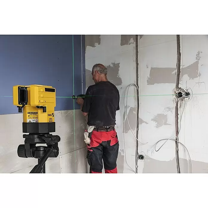 Stabila Kreuzlinienlaser LAX 50 G - Max. Arbeitsbereich: 30 m - Gelber Laser-Nivellier projiziert grüne Linien an eine Wand, bei Bauarbeiten von einer Person benutzt.