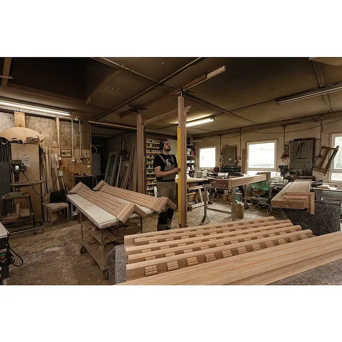 Stabila Wasserwaage 80 AS-2 - Länge: 180 cm, Anzahl Libellen: 3 Stk. - Werkstattansicht mit Holzelementen und einem Handwerker, der ein hölzernes Bauteil mit einer Wasserwaage ausrichtet.