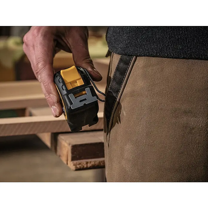 Stabila Taschenbandmaß BM 300 - 5 m - Nahaufnahme eines DeWalt-Maßbandes mit gelbem Akzent, das an einer Arbeitshose befestigt ist. Ideal für präzise Messungen.