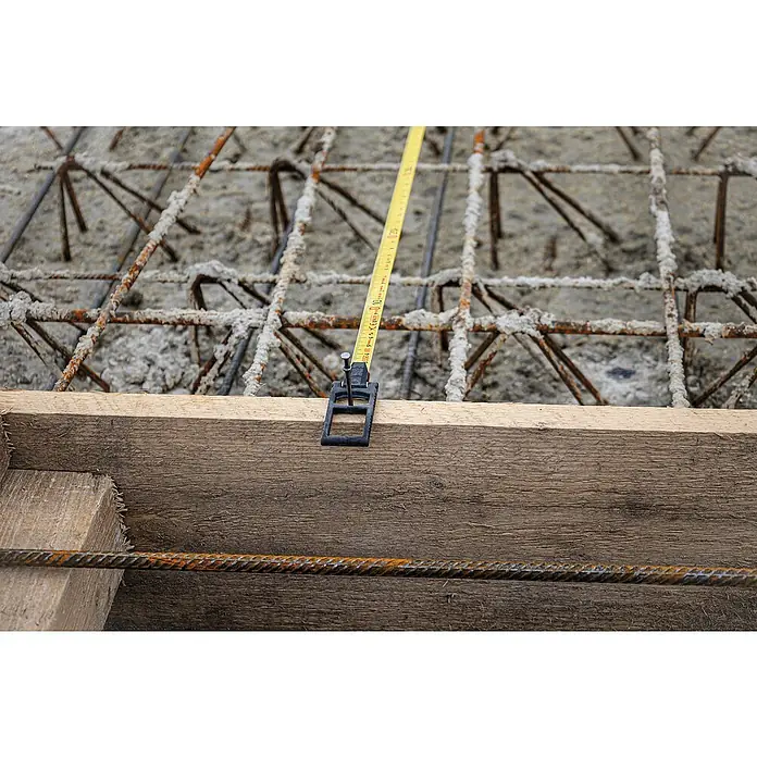 Stabila Kapselbandmaß LBM 2000 Steel 20 m20 m - Nahaufnahme eines gelben Messbandes, das an einer schwarzen Halterung an einem Holzbrett befestigt ist, mit Bewehrungsstahl im Hintergrund.
