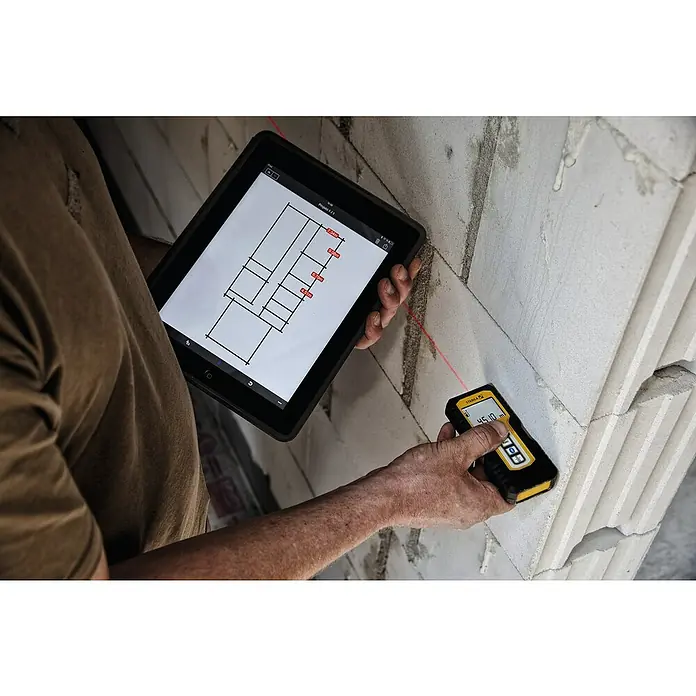 Stabila Laserentfernungsmesser LD 250 BT - Max. Arbeitsbereich: 50 m - Ein Bauarbeiter misst eine Mauer mit einem Stabila Laser-Entfernungsmesser, während er einen Bauplan auf einem Tablet betrachtet.