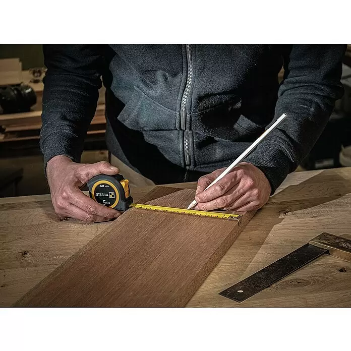 Stabila Taschenbandmaß BM 100 - 5 m - Eine Person misst und markiert Holz mit einem schwarzen und gelben STABILA Maßband.