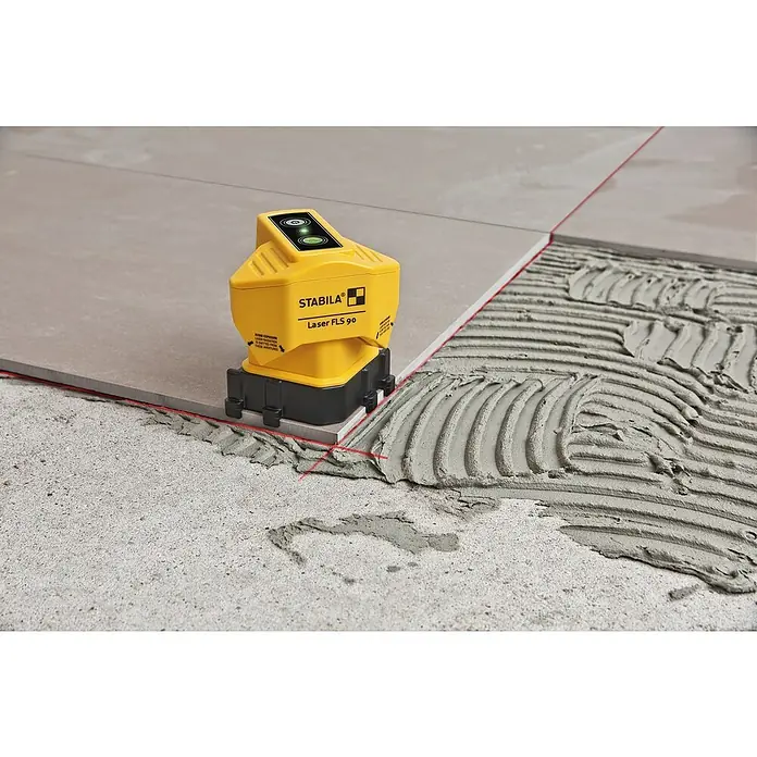 Stabila Bodenlinien-Laser FLS 90 - Ca. 15 m, 90 ° - Das Bild zeigt einen gelben Stabila Laser FLS 90, der auf Fliesen mit Mörtel steht und eine rote Laserlinie projiziert.