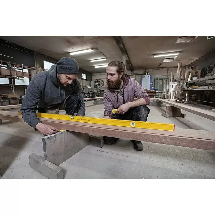 Stabila Wasserwaage Type 80 AS-2 - Länge: 150 cm, Anzahl Libellen: 3 Stk. - Zwei Arbeiter nutzen eine gelbe Wasserwaage, um die Nivellierung eines langen Holzriegels zu prüfen.