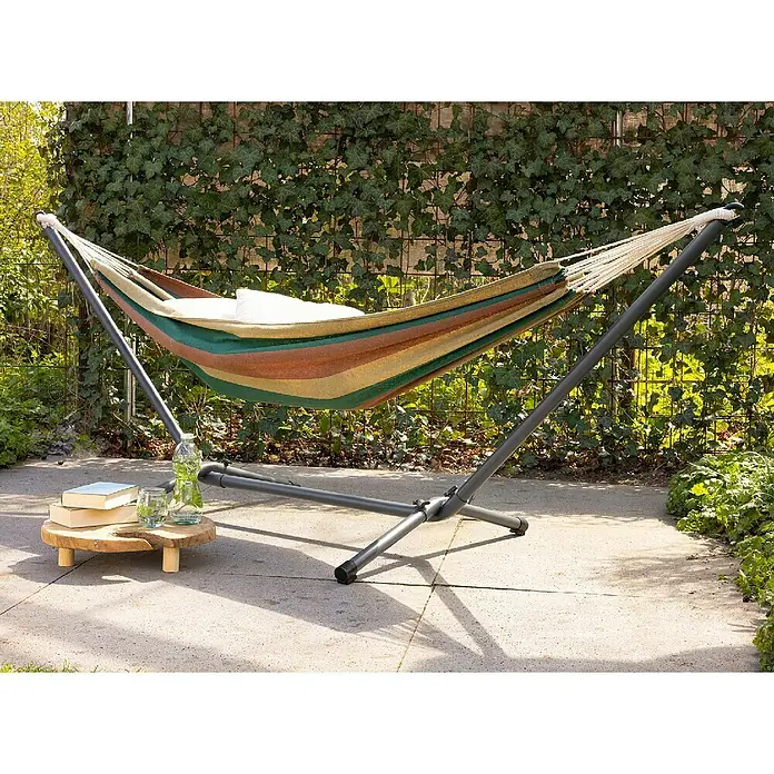 Hamaca individual Haití - L x An: 200 x 100 mm, Colores surtidos - Primer plano de una hamaca de rayas con estructura gris, instalada al aire libre en un patio con mesa de madera y libros.