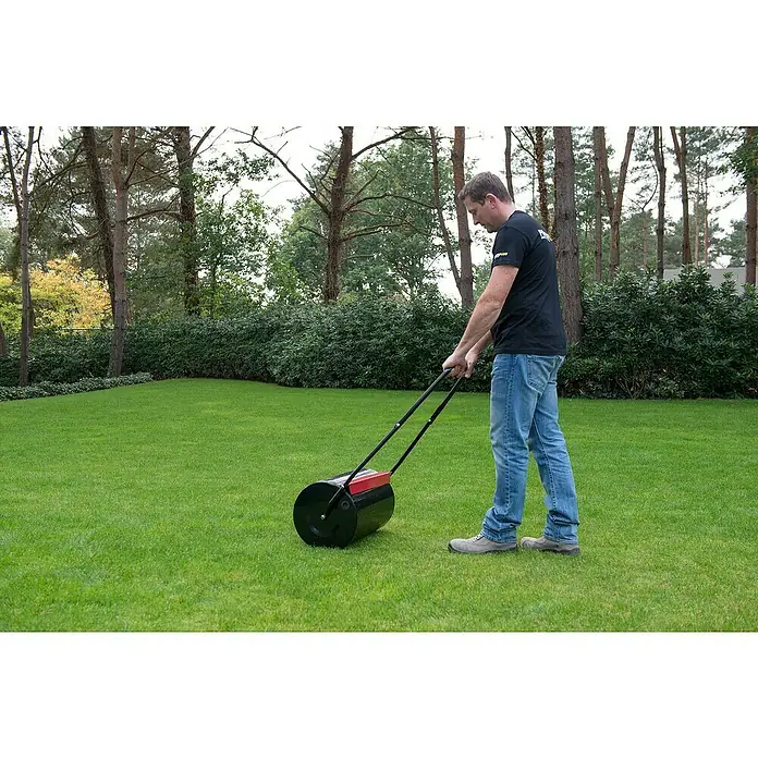 Kreator Rodillo para césped KRTGR9101 - Ancho: 50 cm, Metal - Un hombre usa un rodillo de césped para aplanar un césped verde, asegurando un acabado liso y de aspecto profesional.