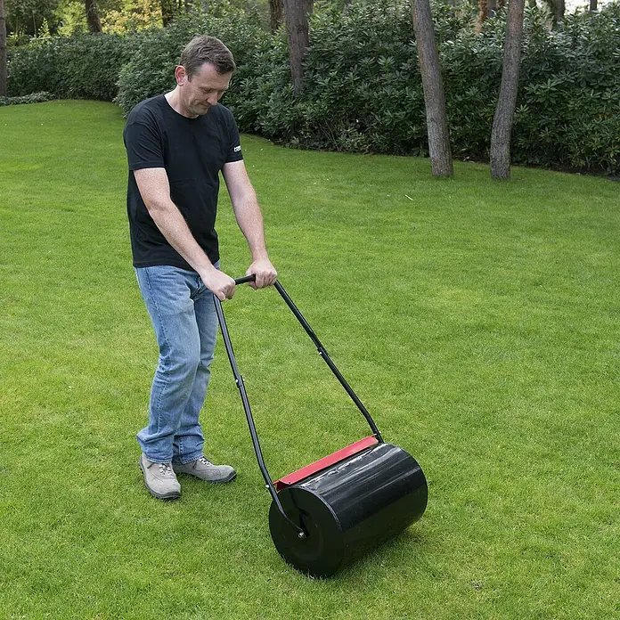 Kreator Rodillo para césped KRTGR9101 - Ancho: 50 cm, Metal - Hombre usando un rodillo de césped para aplanar el césped. El rodillo de césped es negro con un acento rojo y tiene un mango negro.