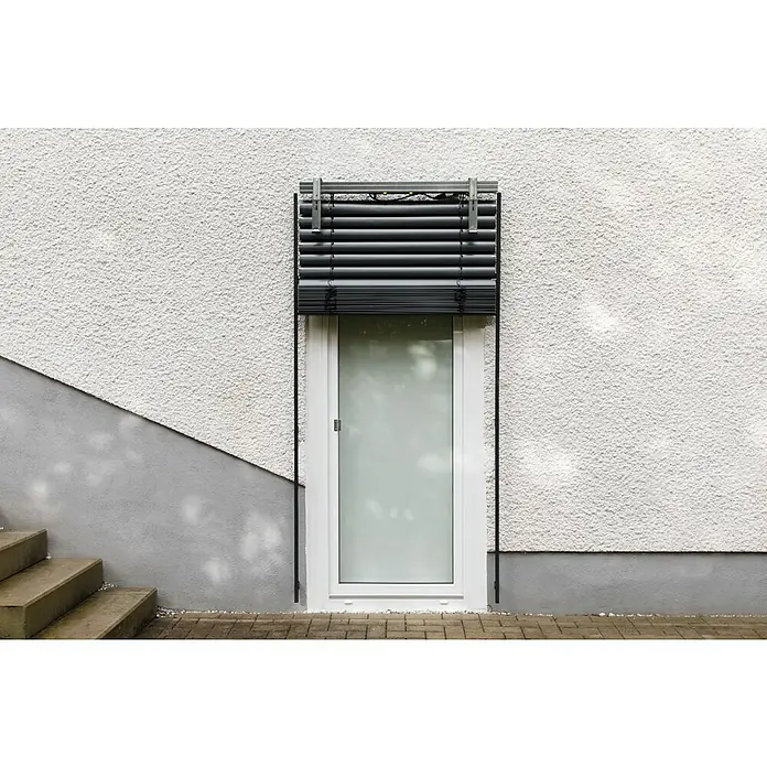 Schellenberg Raffstore Express - 140 x 260 cm - Das Bild zeigt ein Fenster mit einem Rollo, das teilweise heruntergelassen ist und das Licht blockiert. Die Fassade ist weiß und rau.