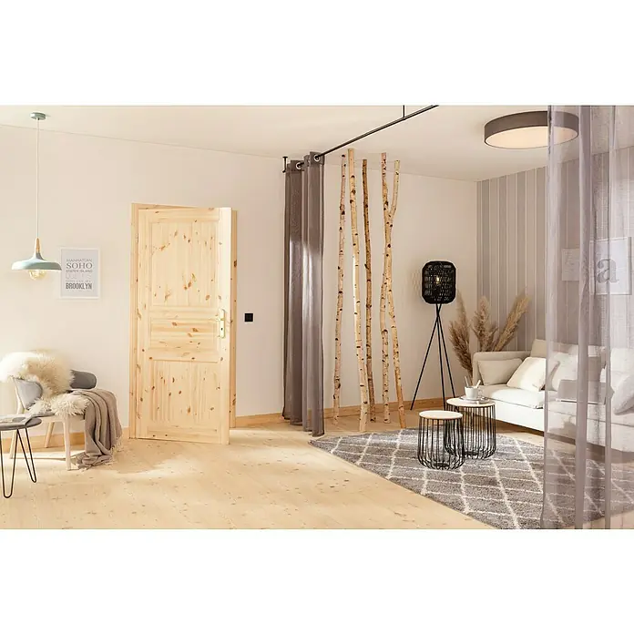 Kilsgaard Landhaustür 02/03 - 610 x 1.985 mm, DIN Anschlag: Links, Kiefer natur - Ein heller Raum mit Holzboden, einer Holztür und dekorativen Birkenstämmen als Raumteiler. Eine gemütliche Sitzecke mit Teppich lädt zum Verweilen ein.