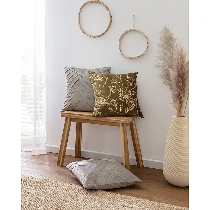 Kissen Fiona - Military Olive, 45 x 45 cm, 100 % Polyester - Einrichtungsszene mit dekorativen Kissen in Grau und Olivgrün auf einer Holzbank, ergänzt durch Wanddekoration und eine hohe Vase.