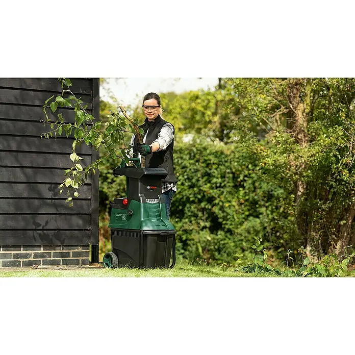 Bosch Elektro-Häcksler AXT 25 TC - Max. Aststärke: 4,5 cm, 2.500 W - Eine Frau benutzt einen Bosch Gartenhäcksler im Freien. Das Gerät zerkleinert Äste und Gartenabfälle effizient.