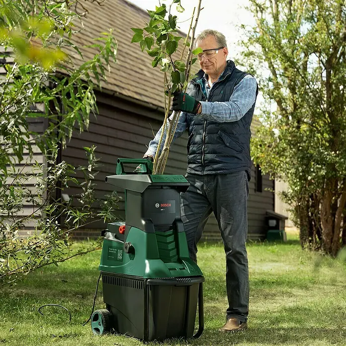 Bosch Elektro-Leisehäcksler AXT 25 D - Max. Aststärke: 4 cm, 2.500 W - Ein Mann benutzt einen Bosch AXT Gartenhäcksler im Garten, um Äste zu zerkleinern.