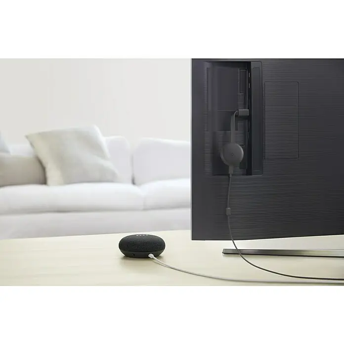 Google Nest Sprachgesteuerter Lautsprecher Mini - Carbon, Netzbetrieben, Kabellänge: 1,5 m - Das Bild zeigt einen Google Nest Mini und einen Google Chromecast, die zusammen in einem Wohnzimmer auf einem Tisch platziert sind.