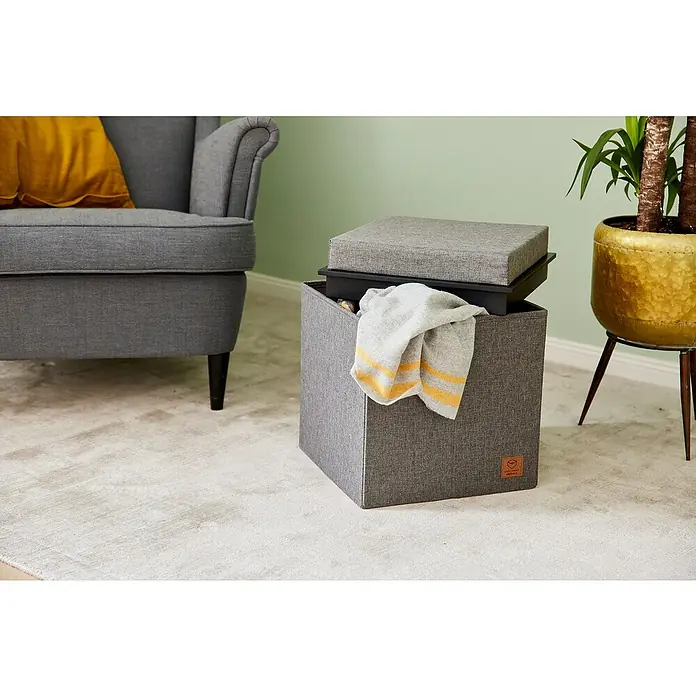 Store It Premium Sitzhocker - L x B x H: 37 x 37 x 41 cm, Grau - Grauer Ottoman-Aufbewahrungswürfel mit abnehmbarem Deckel und einem grauen Sessel im Hintergrund.