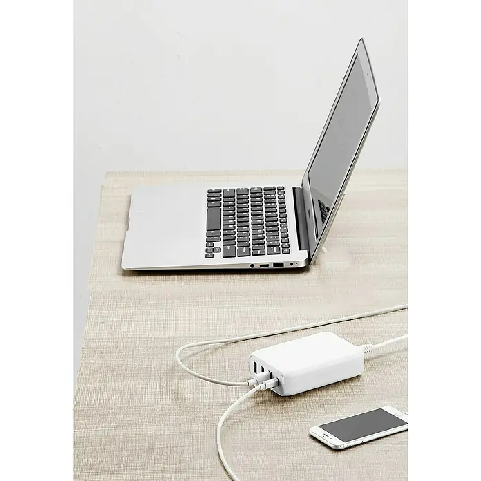 BAUHAUS USB-Ladegerät Quick Charger - 4-fach, Weiß, USB-A-Buchse, USB-C-Buchse, Max. Leistung: 45 W - Laptop, Ladegerät und Smartphone auf einem Tisch. Das Ladegerät lädt sowohl das Laptop als auch das Smartphone gleichzeitig auf.